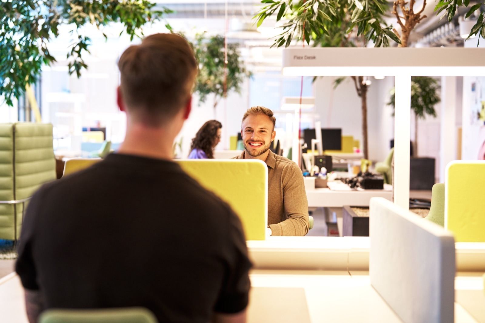 André at a desk in a bright open-plan office with plants