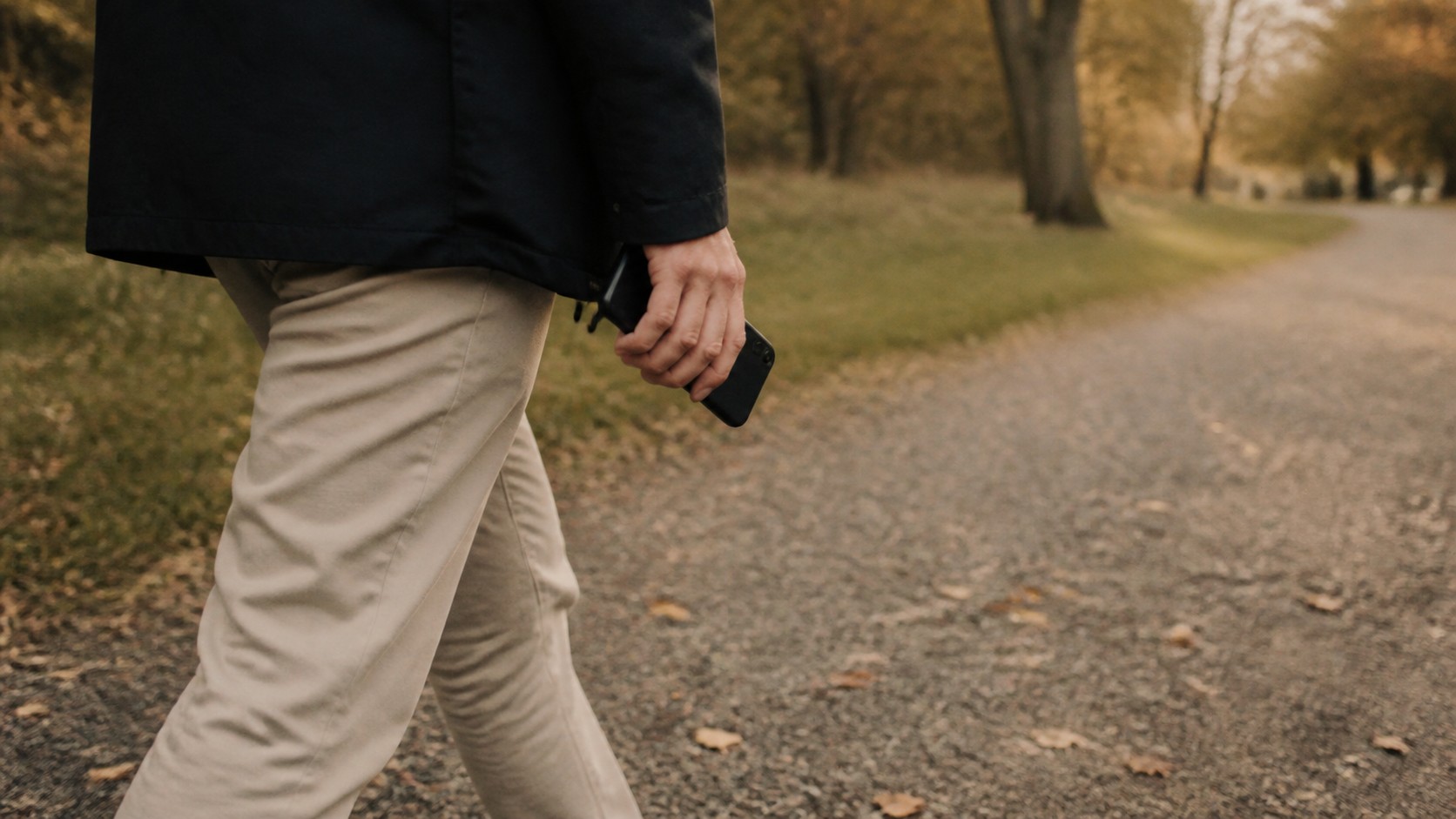 Person på promenad längs en grusväg med mobilen i handen